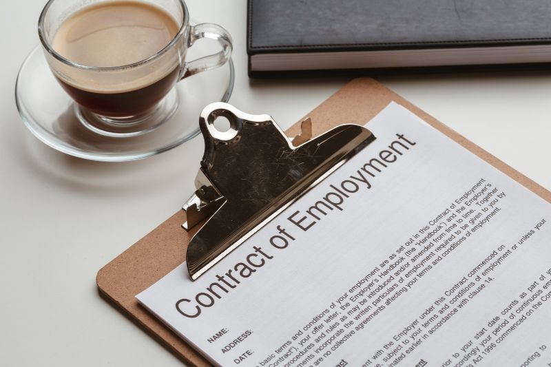 Employment contract on a clipboard beside a coffee cup and notebook, representing formal hiring terms and conditions